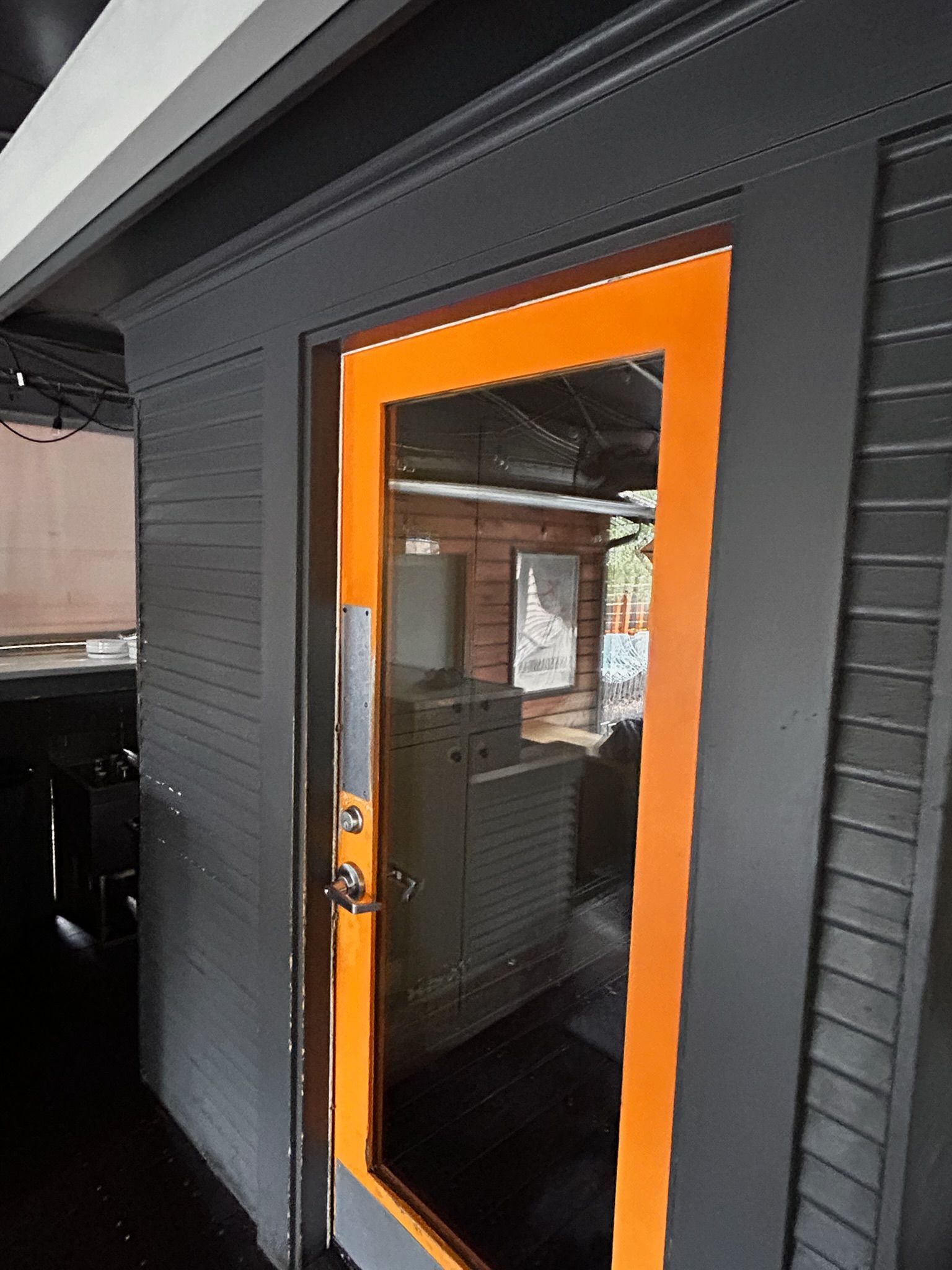 Black building exterior with orange door frame around glass door; interior visible.