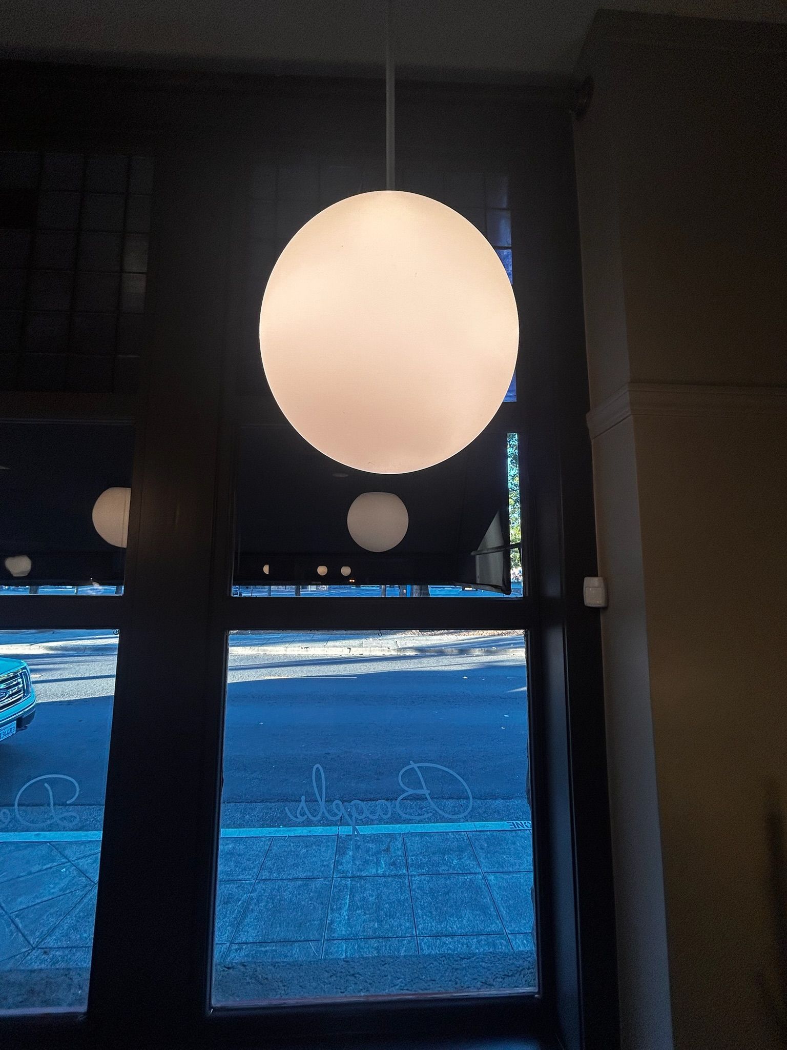 Large white globe-shaped pendant light hanging in front of a window. Exterior scene visible.