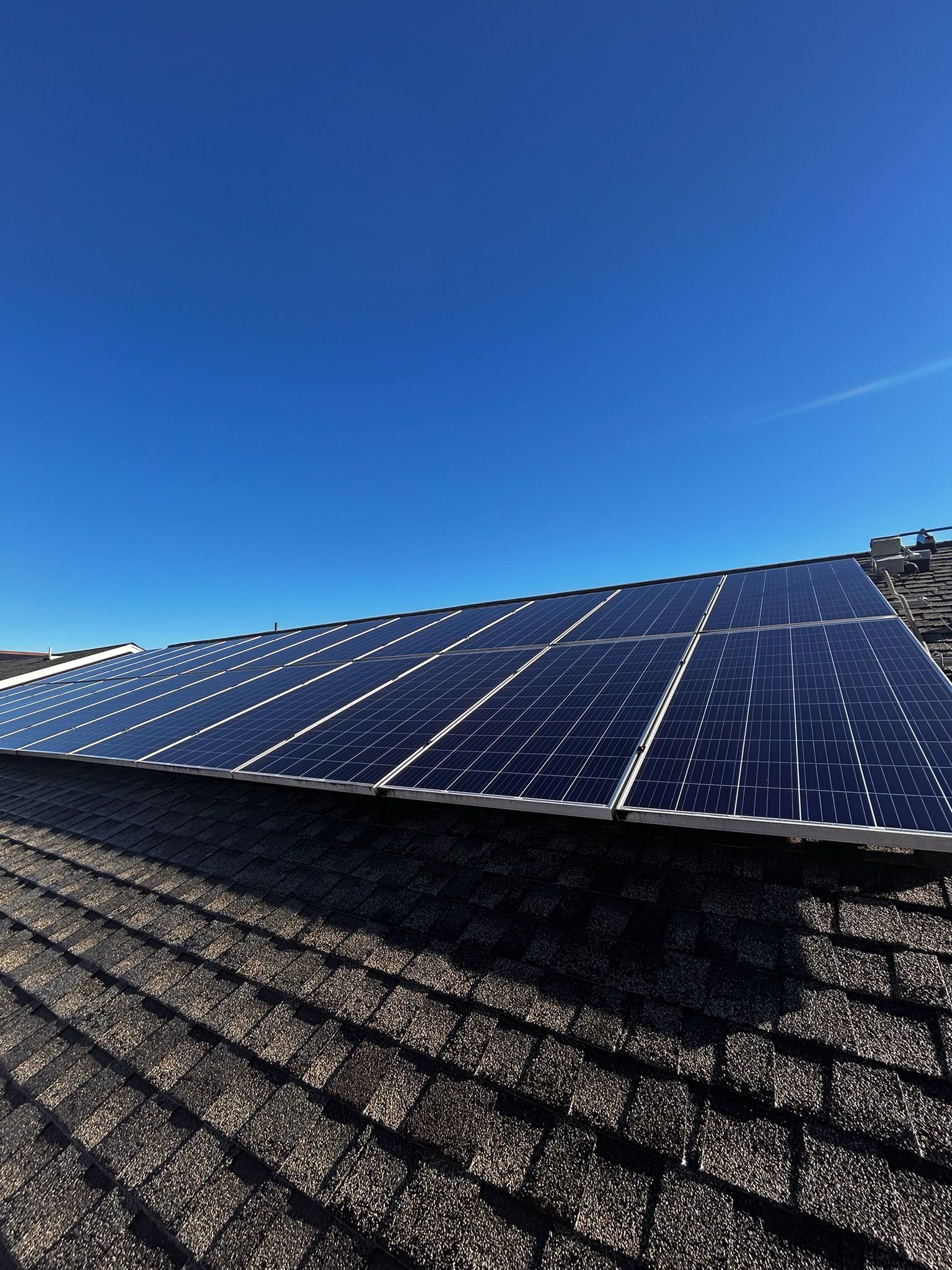 Solar panels installed on a dark, shingled roof against a bright blue sky.