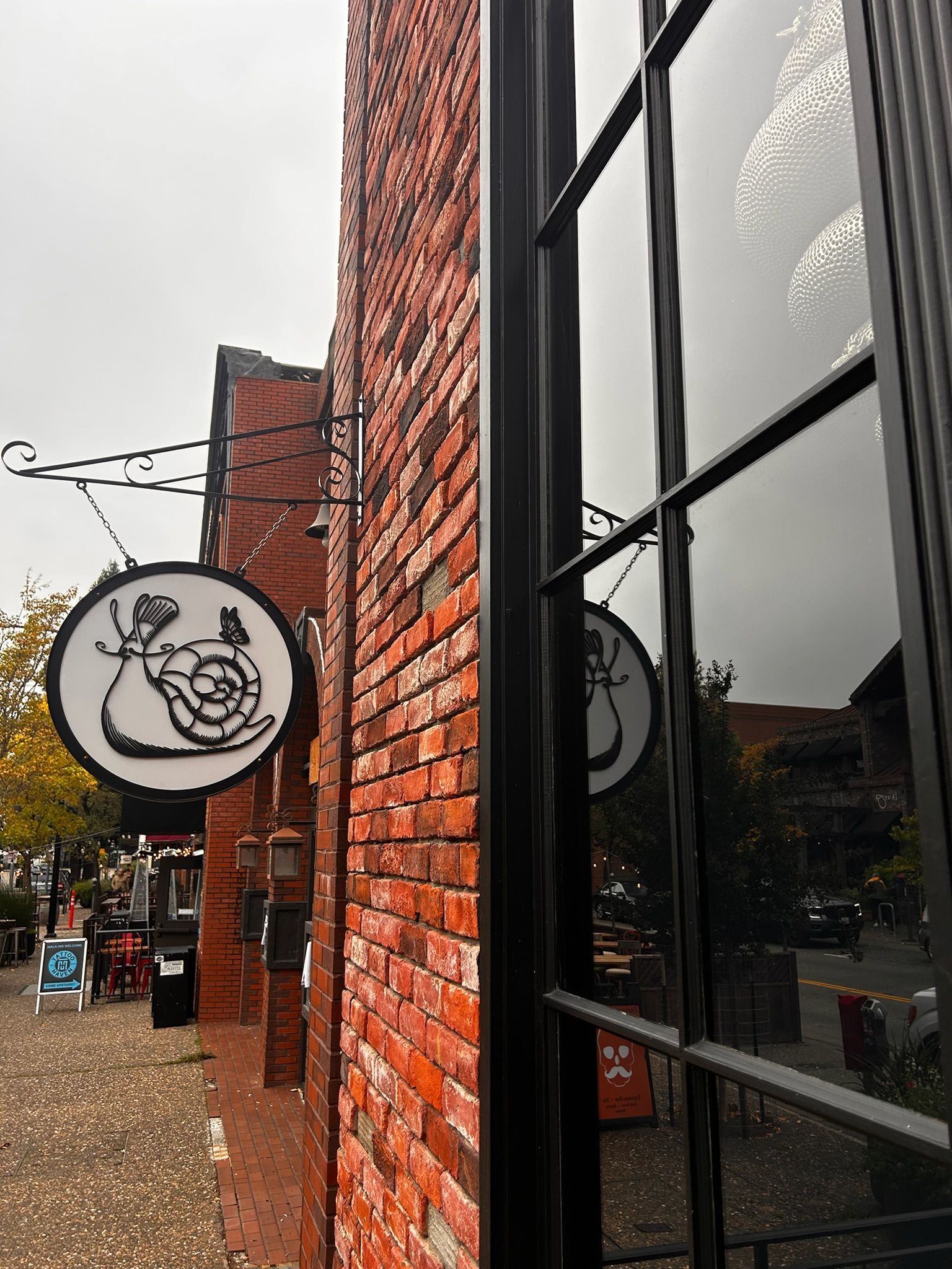 Brick building with a circular sign of a snail. The sign is reflected in a window.