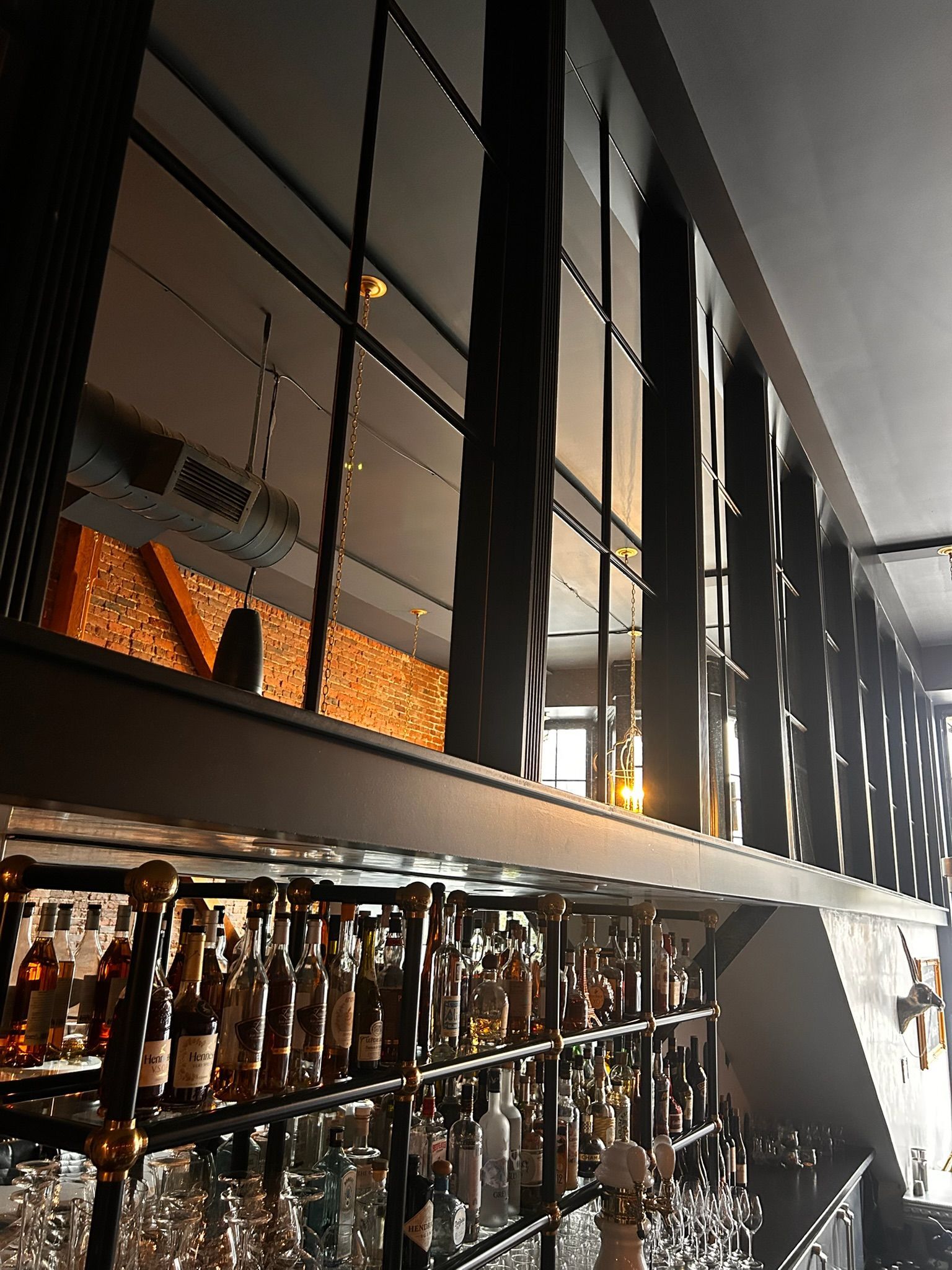 Interior view of a bar with liquor bottles on shelves, a mezzanine, and black metal beams.