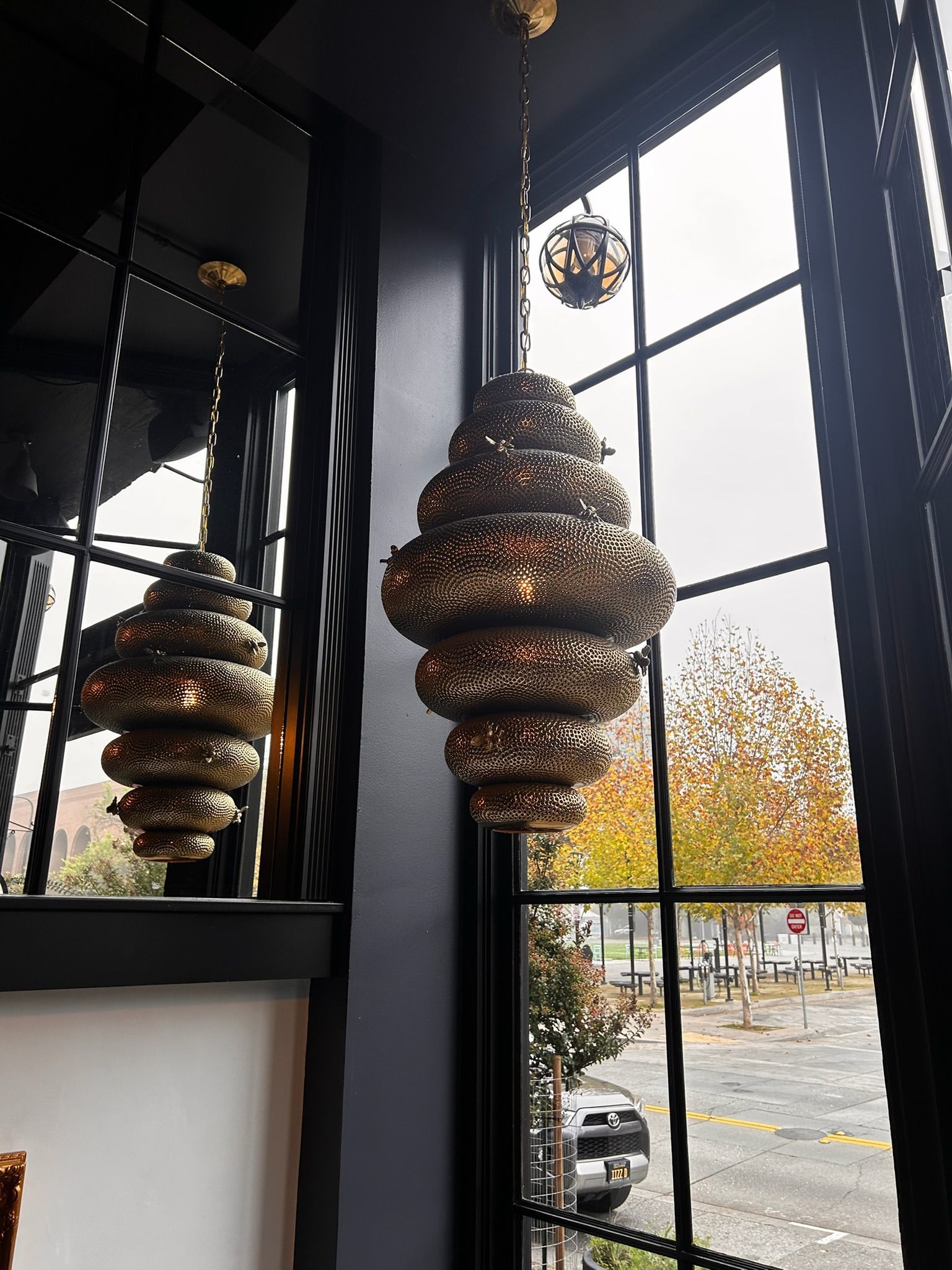 Two ornate gold pendant lights hanging near a window, street view visible.
