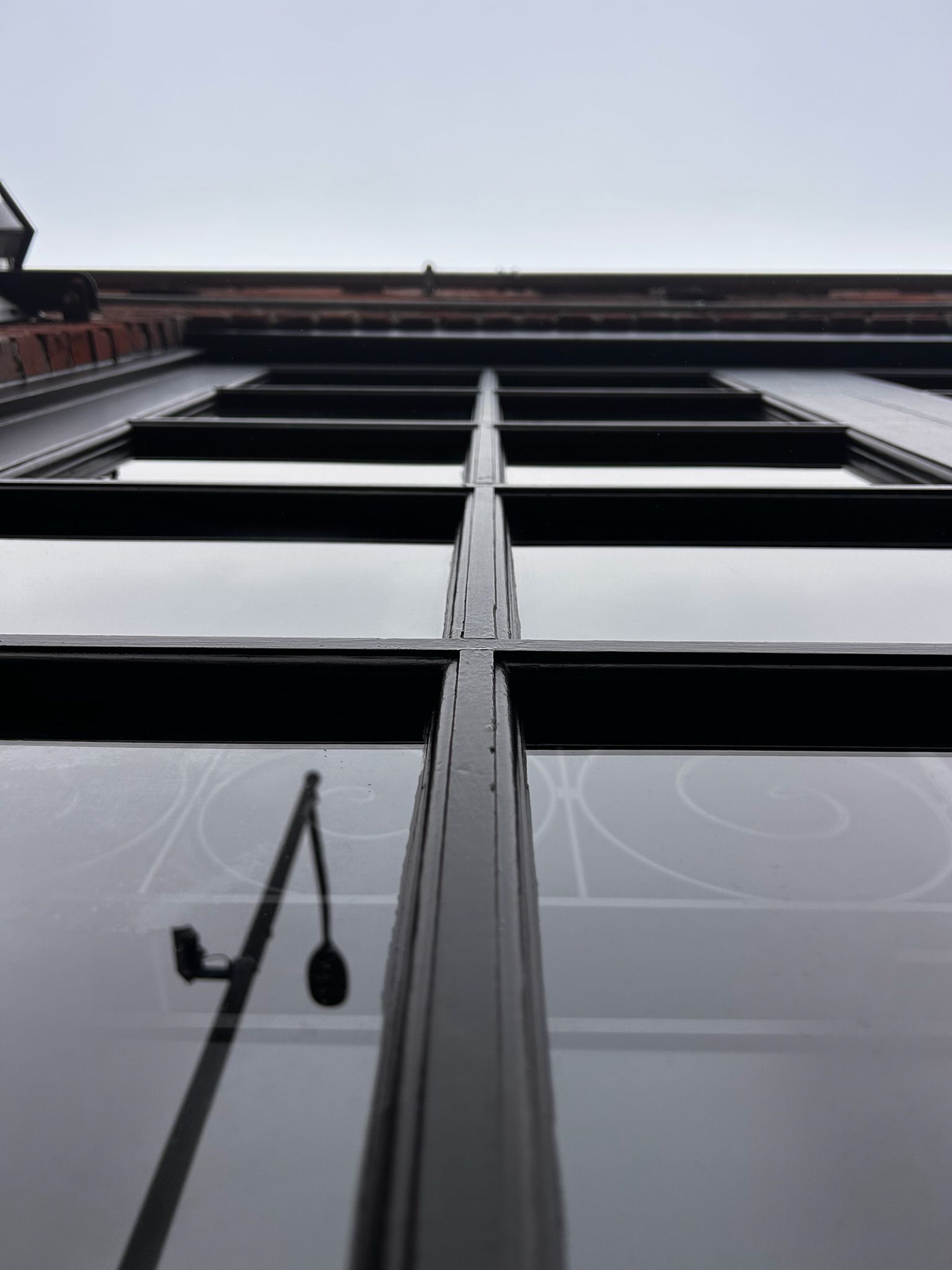 Looking up at a window with black frames, reflecting a street lamp and cloudy sky.
