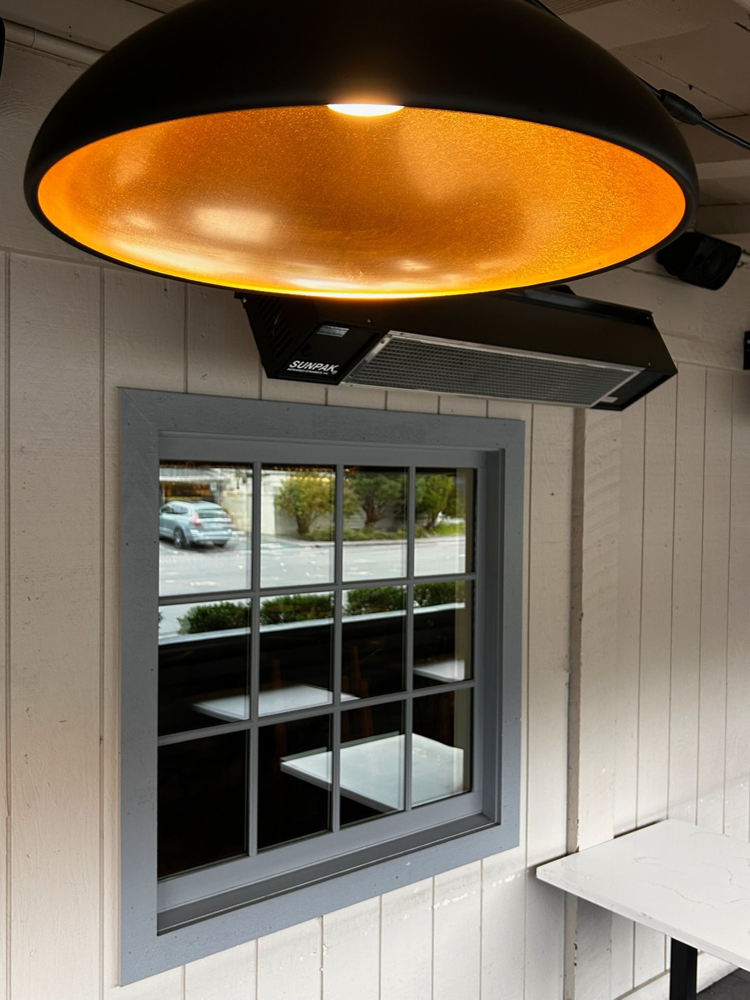 A window reflecting tables and street, under a gold-lined black dome light and range hood.