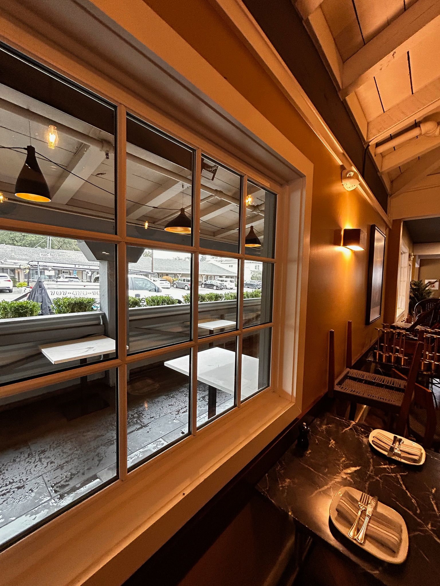 Interior restaurant view with window showing outdoor seating and street. Black marble bar with silverware.