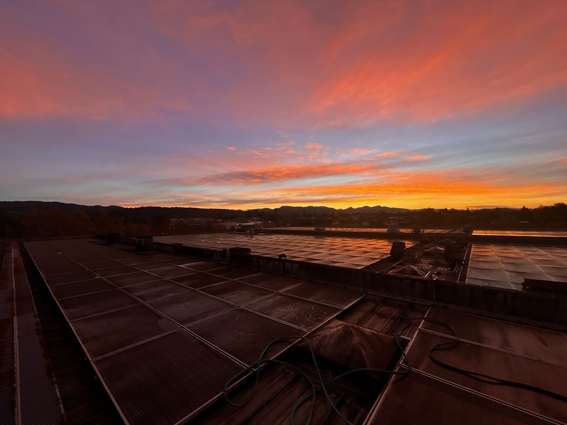 Sunset over a river, orange and pink sky reflected in the water, seen from a dark rooftop.