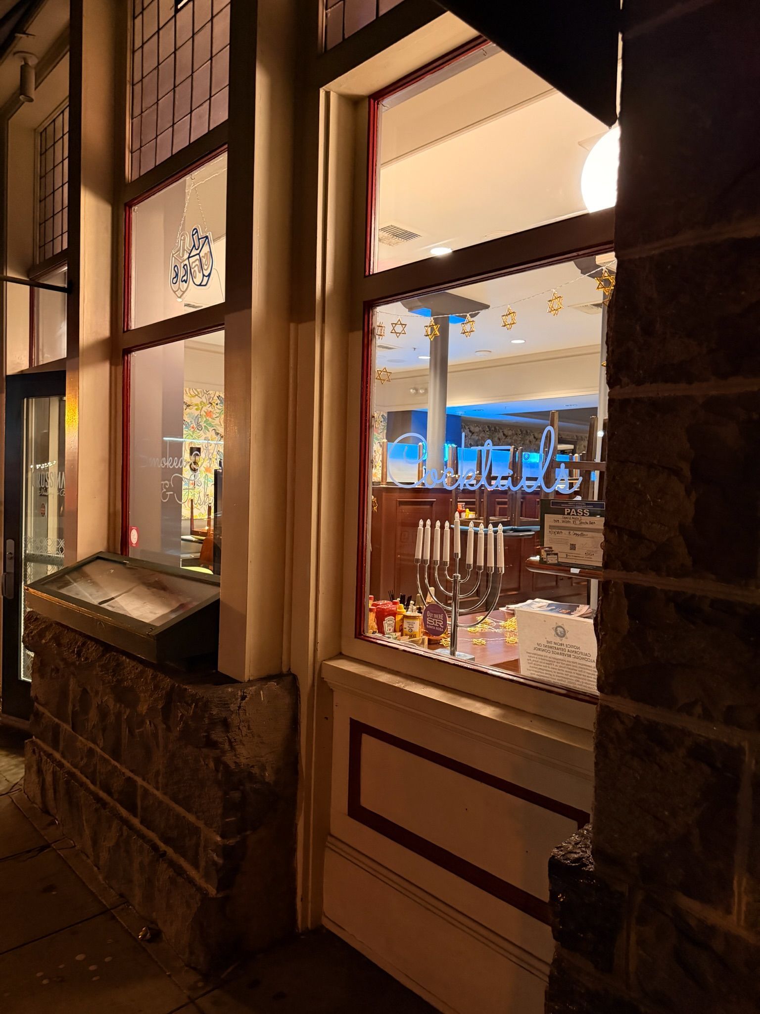 Exterior nighttime view of shop window with interior lit. Stone wall with window frame, and objects inside.