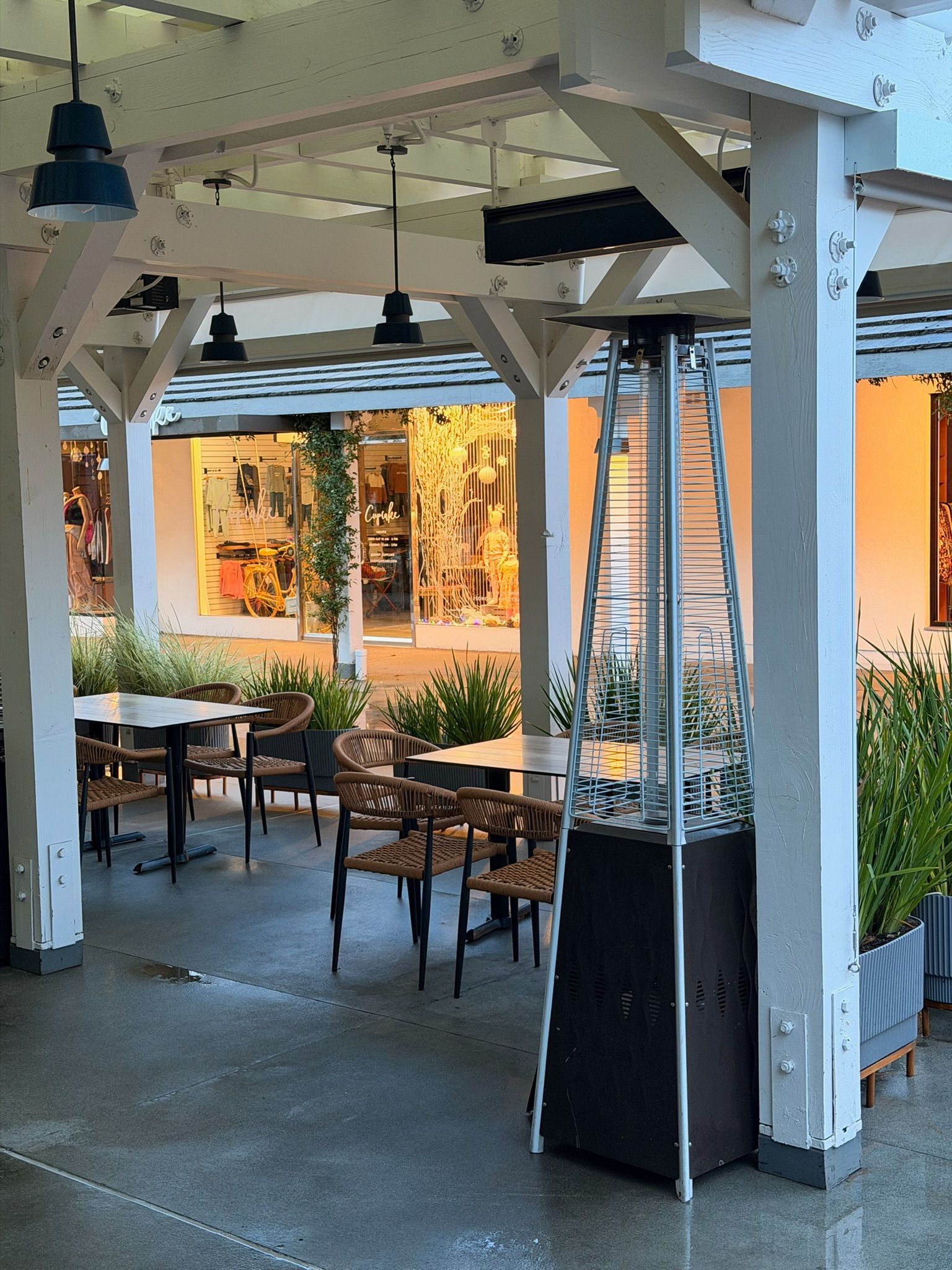Outdoor dining area with patio heater, tables, chairs, and white pergola.