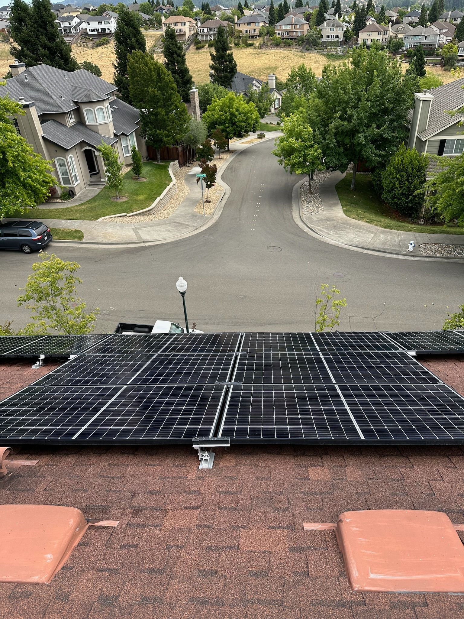 Solar panels on a red-tiled roof with a residential street and houses in the background.