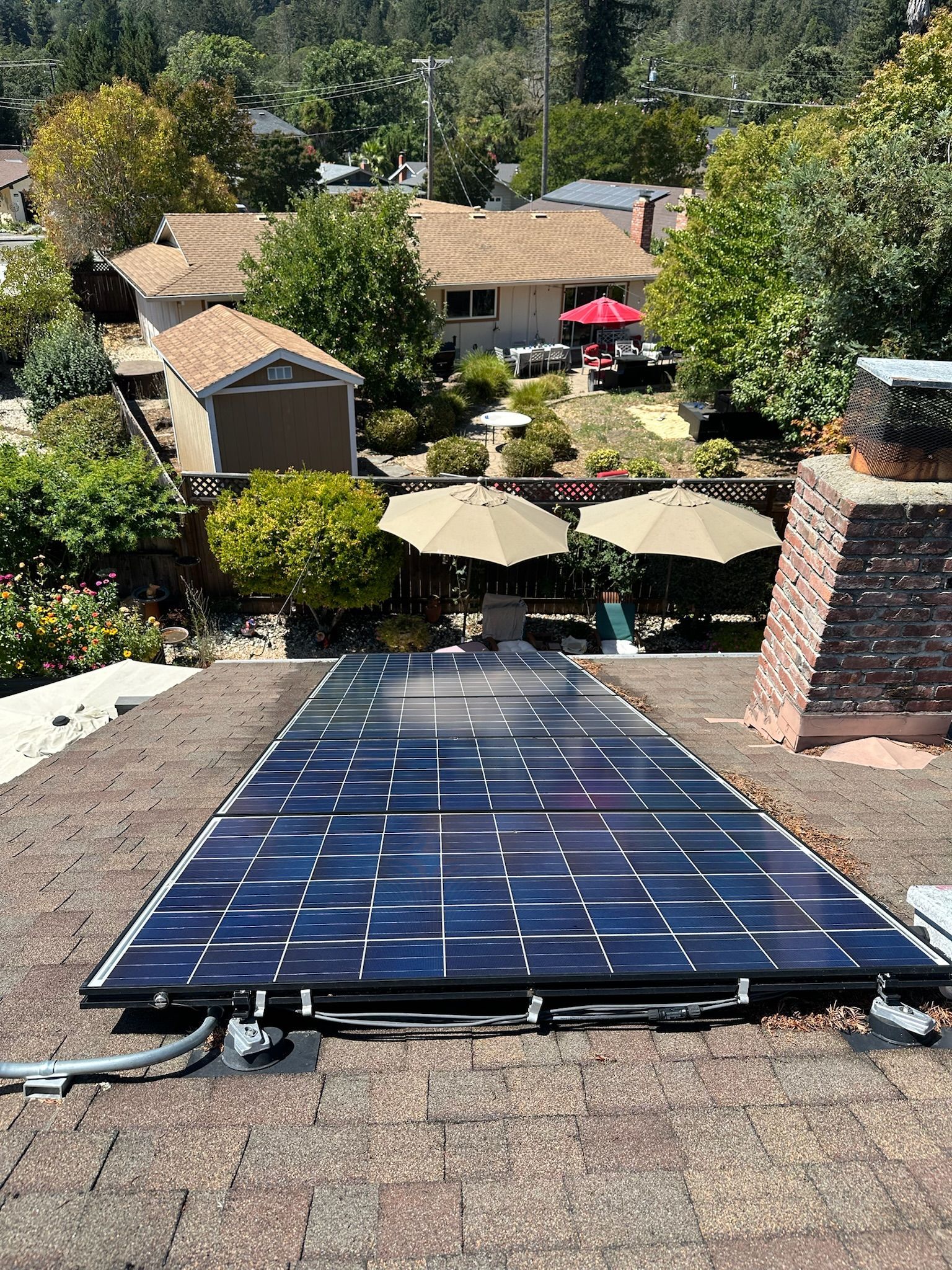 Solar panels installed on a brown-shingled rooftop with a neighborhood background.
