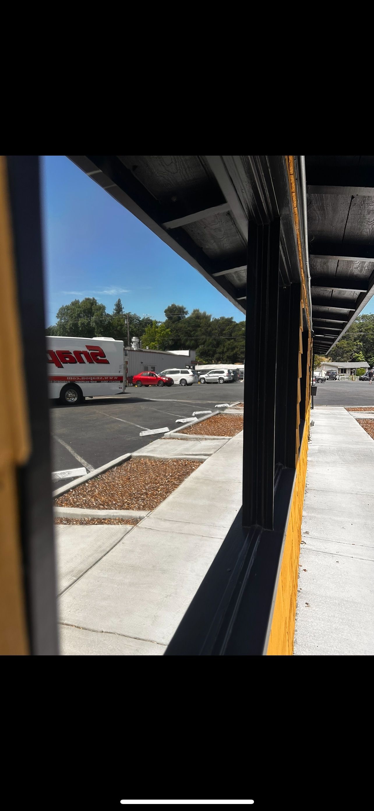 View from a bus shelter, with cars and a truck parked in the distance under a blue sky.