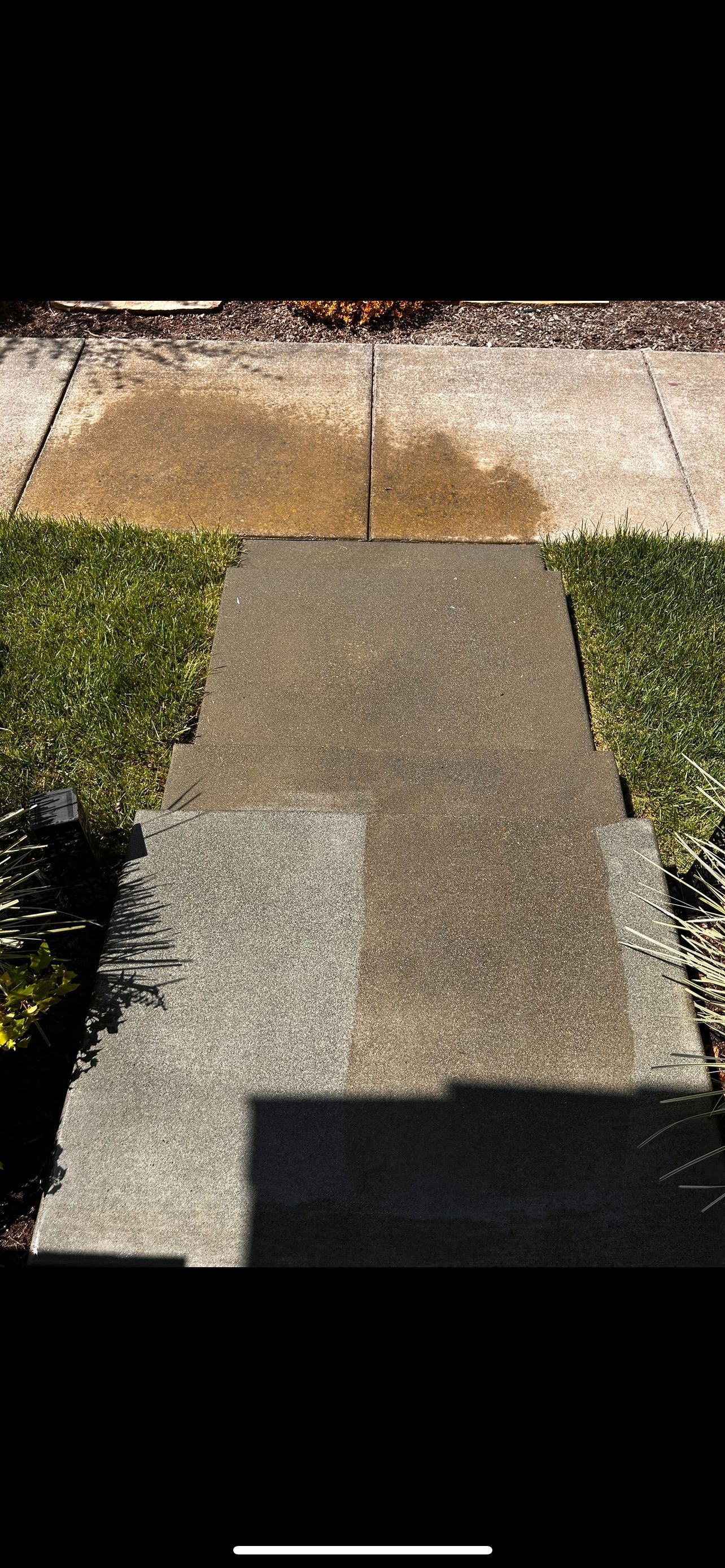 A concrete walkway with a shadow on it, leading to a lawn and sidewalk.
