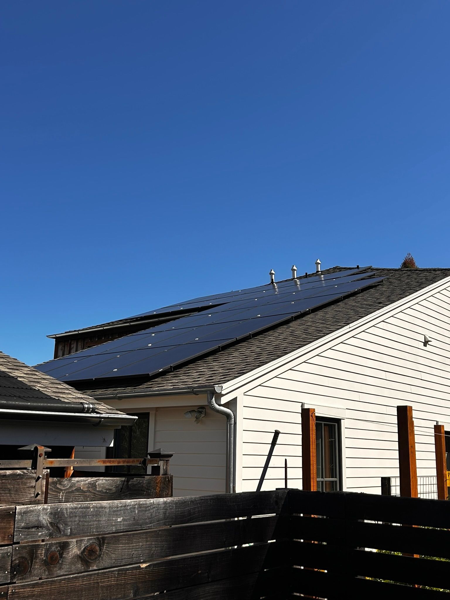 Solar panels on a sloped roof of a white building under a clear blue sky.