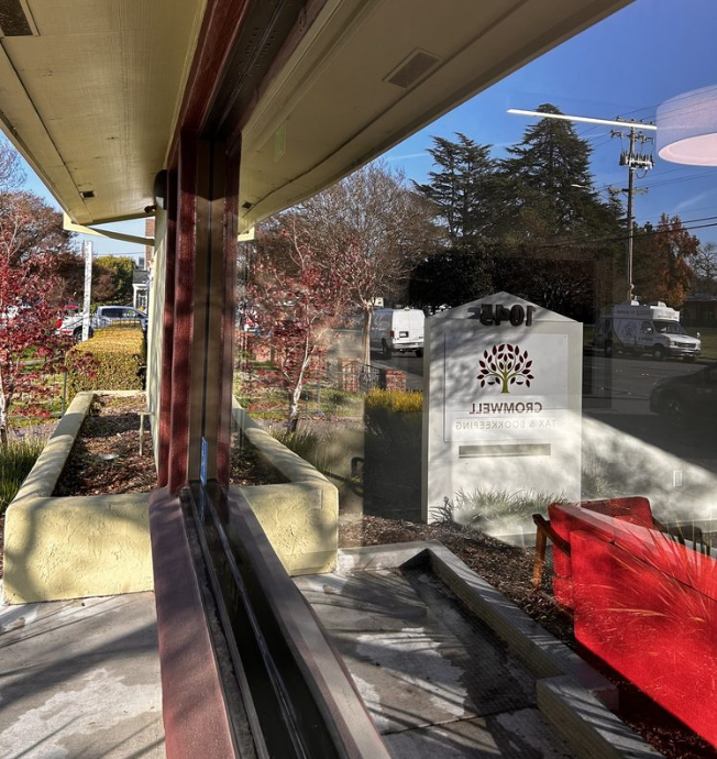 Exterior view through a window, showing a storefront with a sign and the reflected outdoor surroundings.