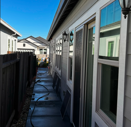 Side exterior of a house with windows, a path, and a wooden fence; blue sky overhead.