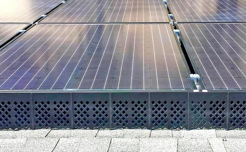 Solar panels installed on a roof, with dark panels and a black barrier at the edge.