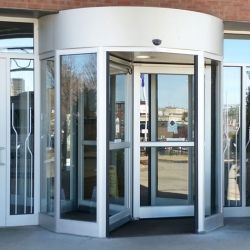 Glass doors of a building entrance with white frames. Includes automatic door opener and welcome mat.