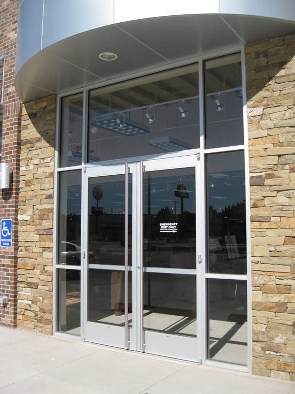 Glass doors with a silver frame, set in a stone building facade, with a wheelchair access sign on the left.