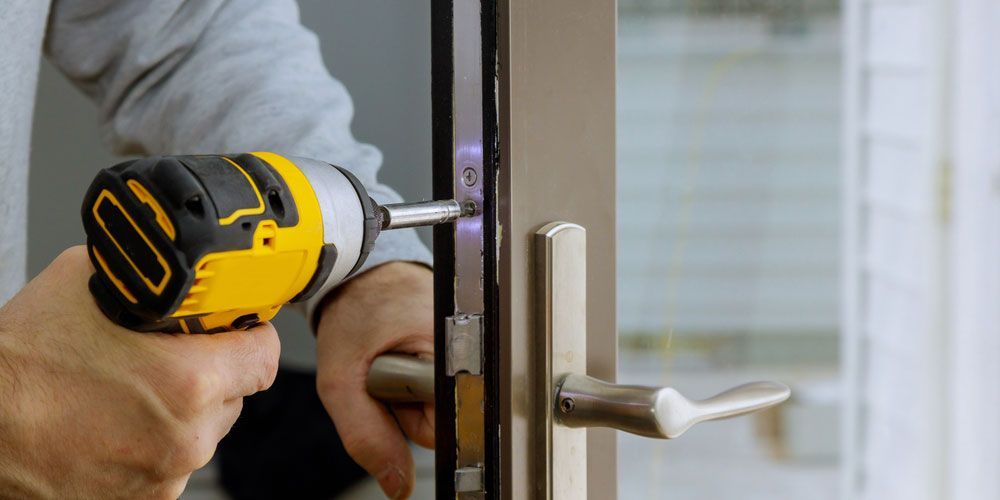 A person using a yellow and black power drill to install a door lock.