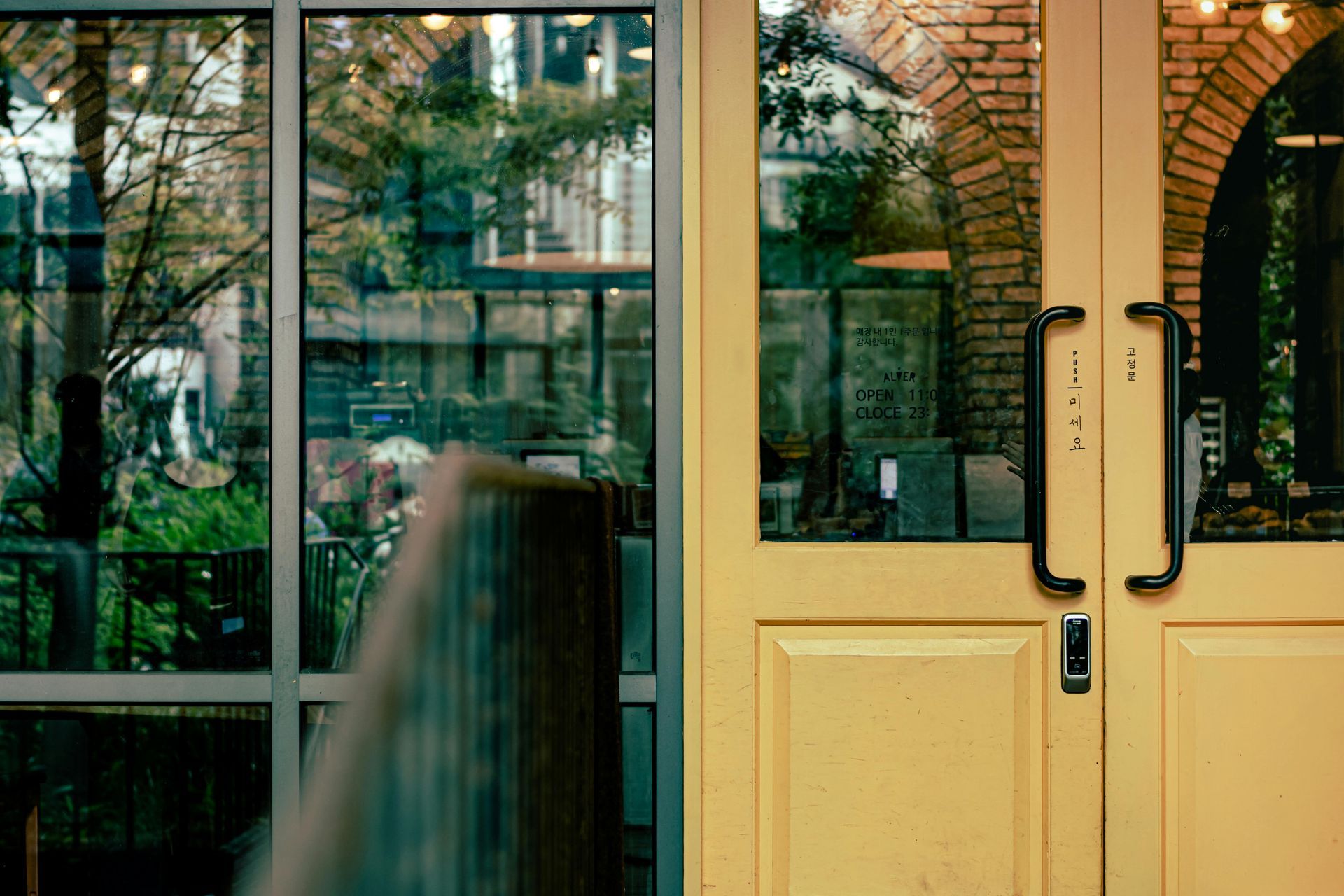 Yellow double doors with black handles beside large glass windows reflecting trees and a building