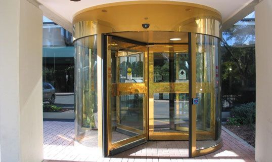 Glass revolving door at a building entrance with a yellow canopy.