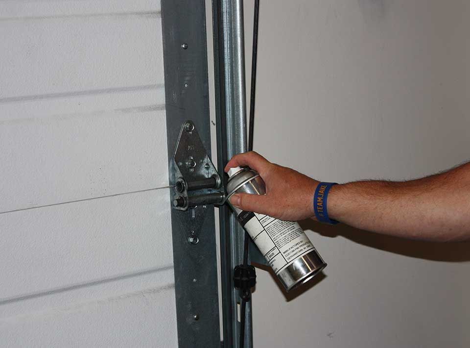 Person spraying lubricant on a garage door hinge.