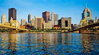 A city skyline over a body of water with a bridge in the foreground.