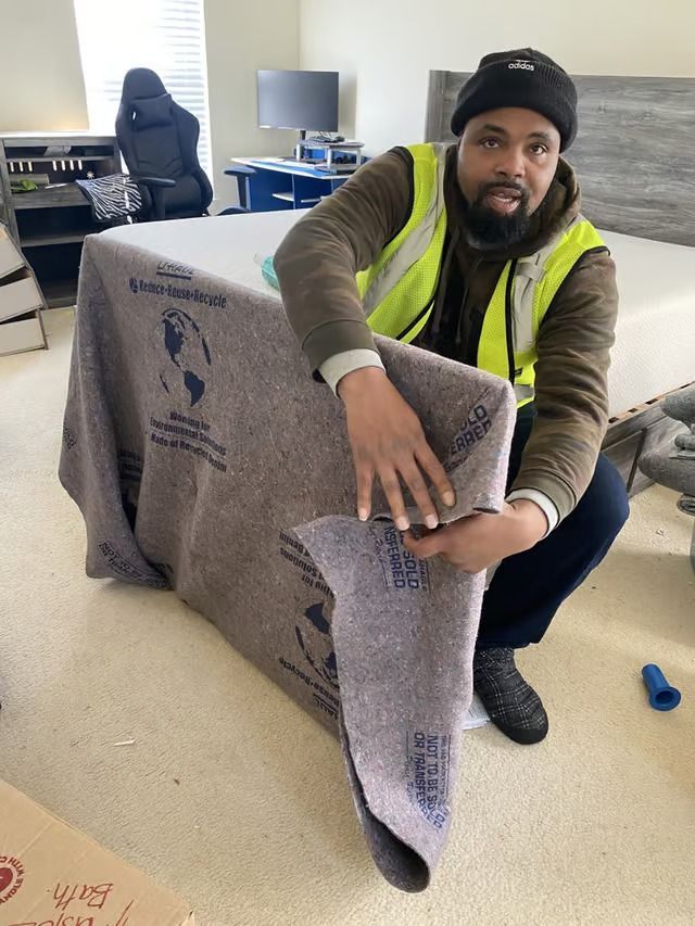 A man in a yellow vest is holding a piece of blanket in a bedroom.
