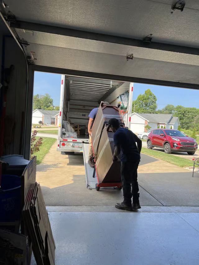 A man is pushing a refrigerator into a truck in a garage.