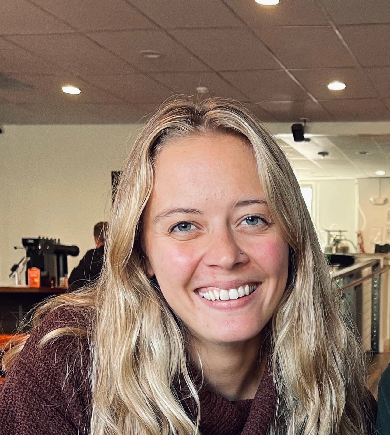Woman with blonde hair and a nose ring smiling in a cafe.
