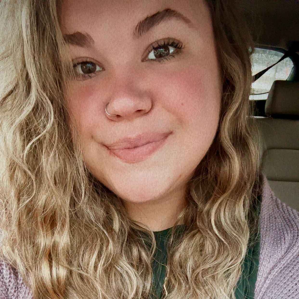 Woman with curly blonde hair and nose ring smiles.