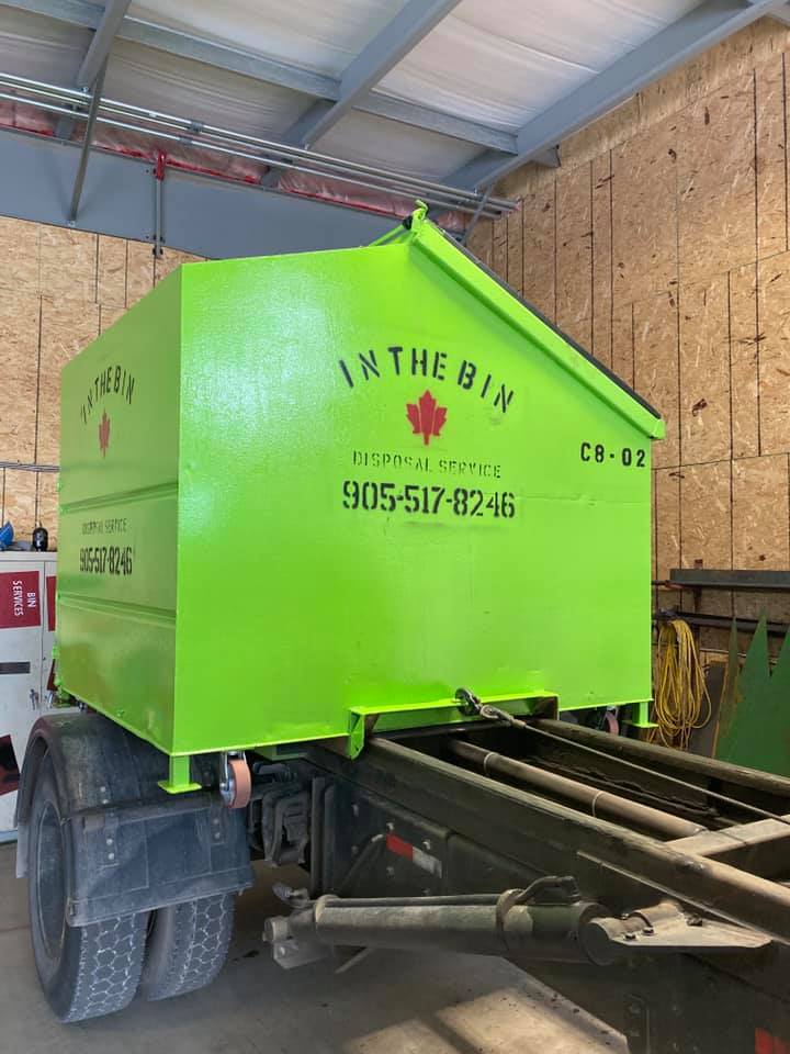 A green dumpster is sitting on the back of a truck.