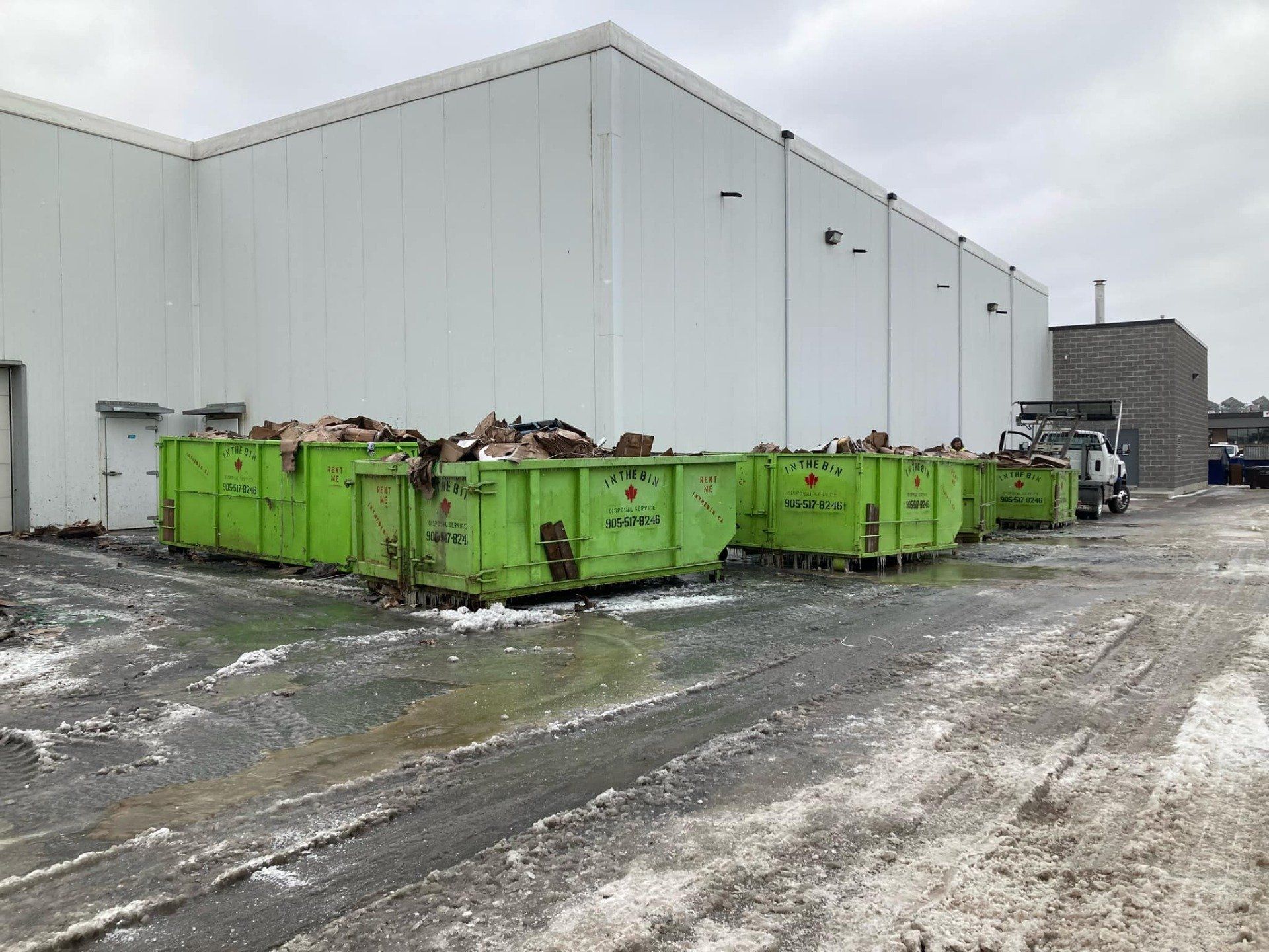 A row of green dumpsters are parked in front of a white building.