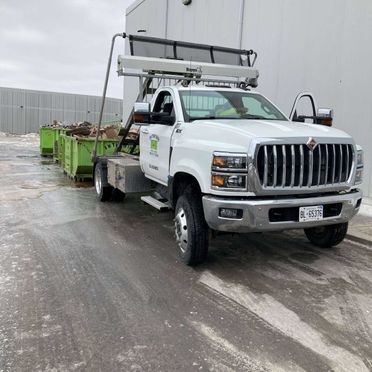 A white truck is parked on the side of the road next to green dumpsters.