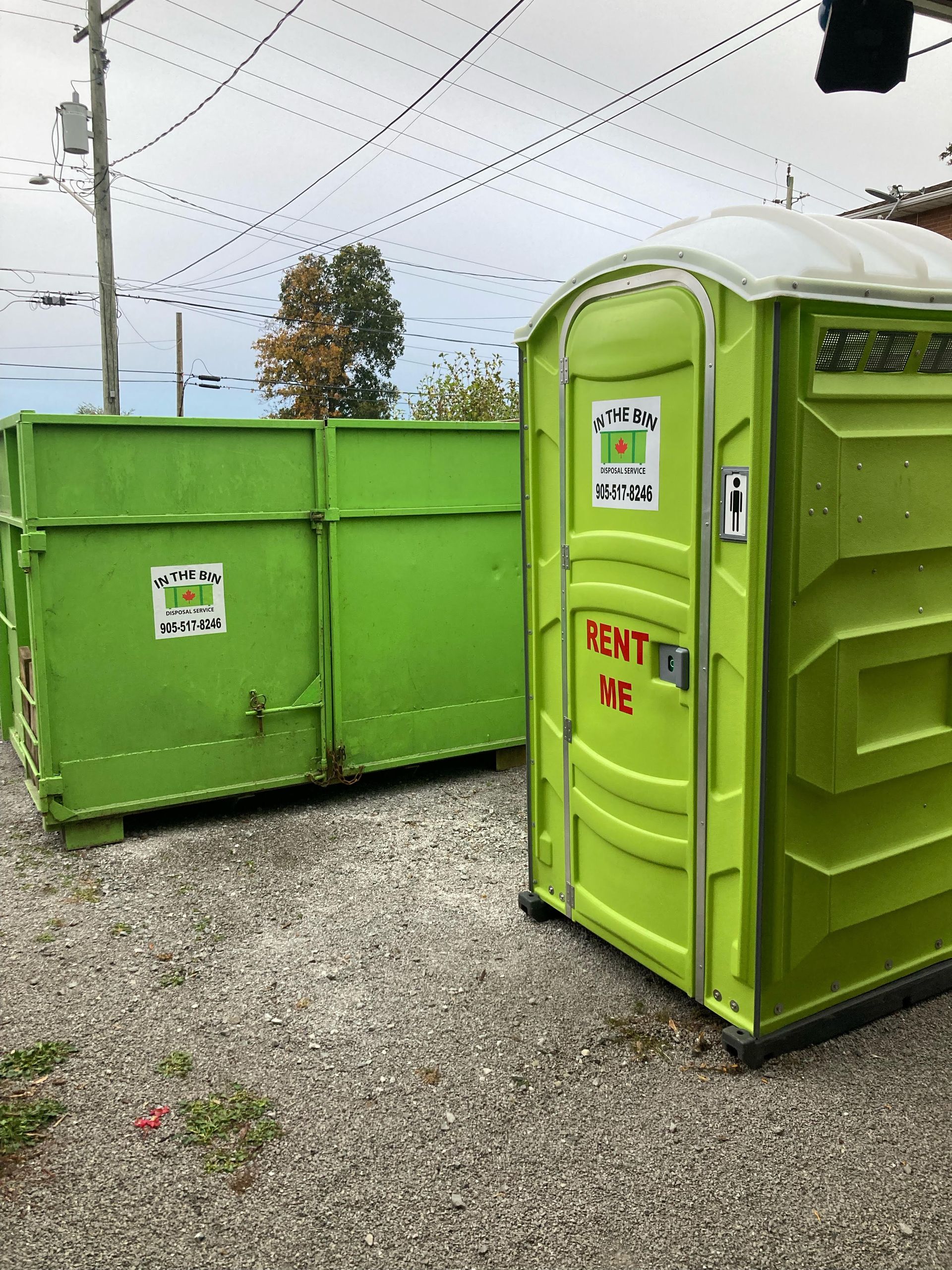 Bright green portable toilet and dumpster on gravel lot; overcast sky.
