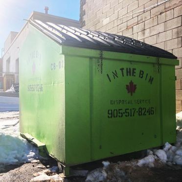 A green dumpster is parked in front of a brick building.