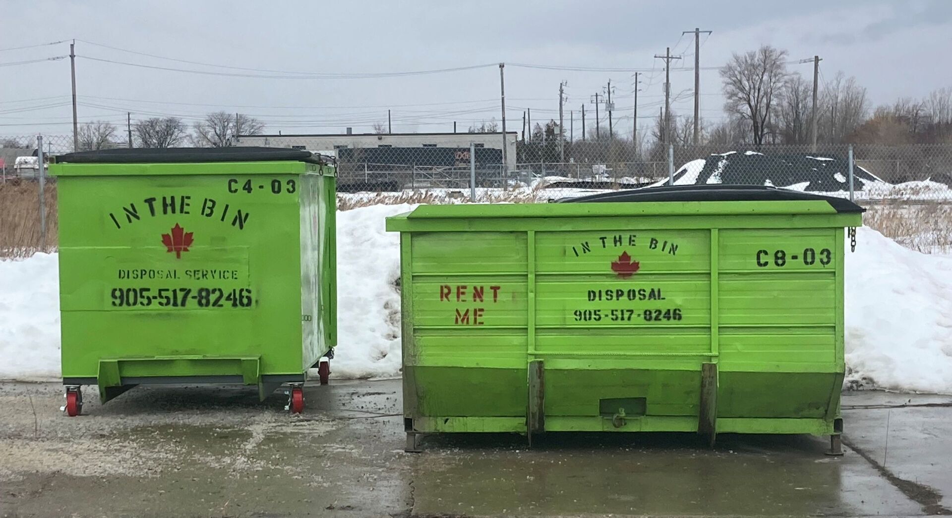 Two green dumpsters are parked next to each other in a parking lot.