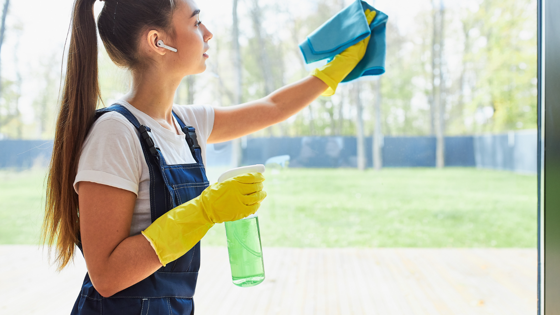 A woman is cleaning a window with a cloth and spray bottle.