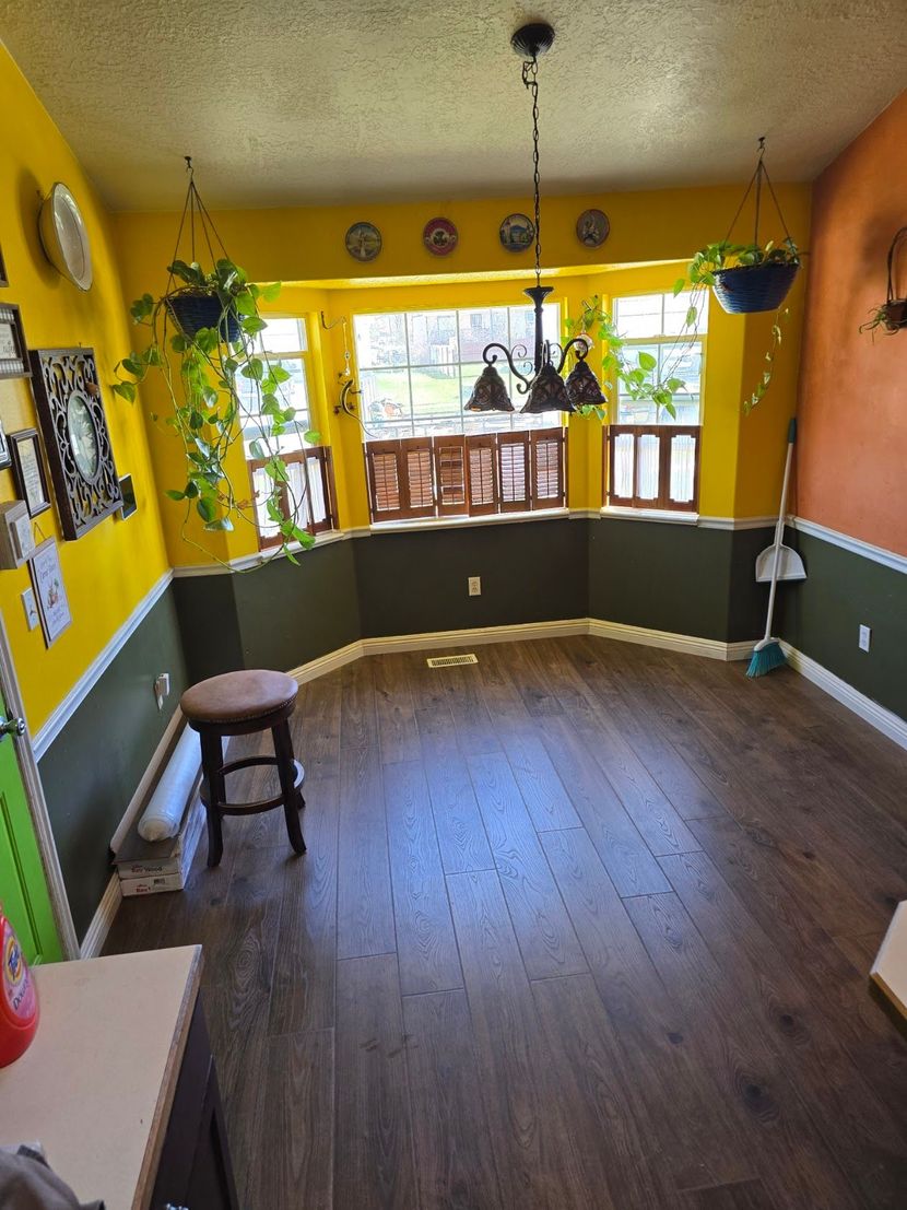Bright yellow dining nook with wooden floor, bay window, hanging plants, and a stool by the wall.