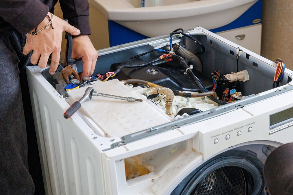 Hands repairing the top of a front-loading washing machine with exposed internal parts