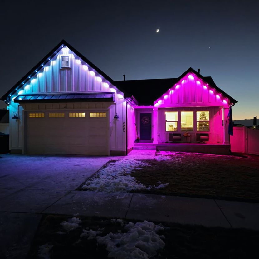 House decorated with blue and pink Christmas lights at night, with snow on the ground