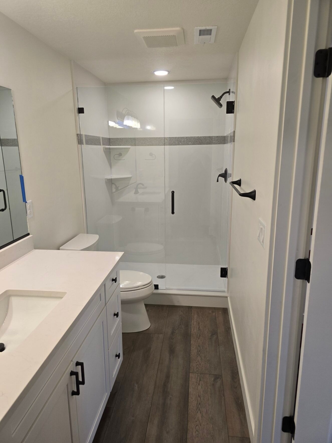 Small white bathroom with tub-shower, toilet, vanity sink, and dark wood floor.