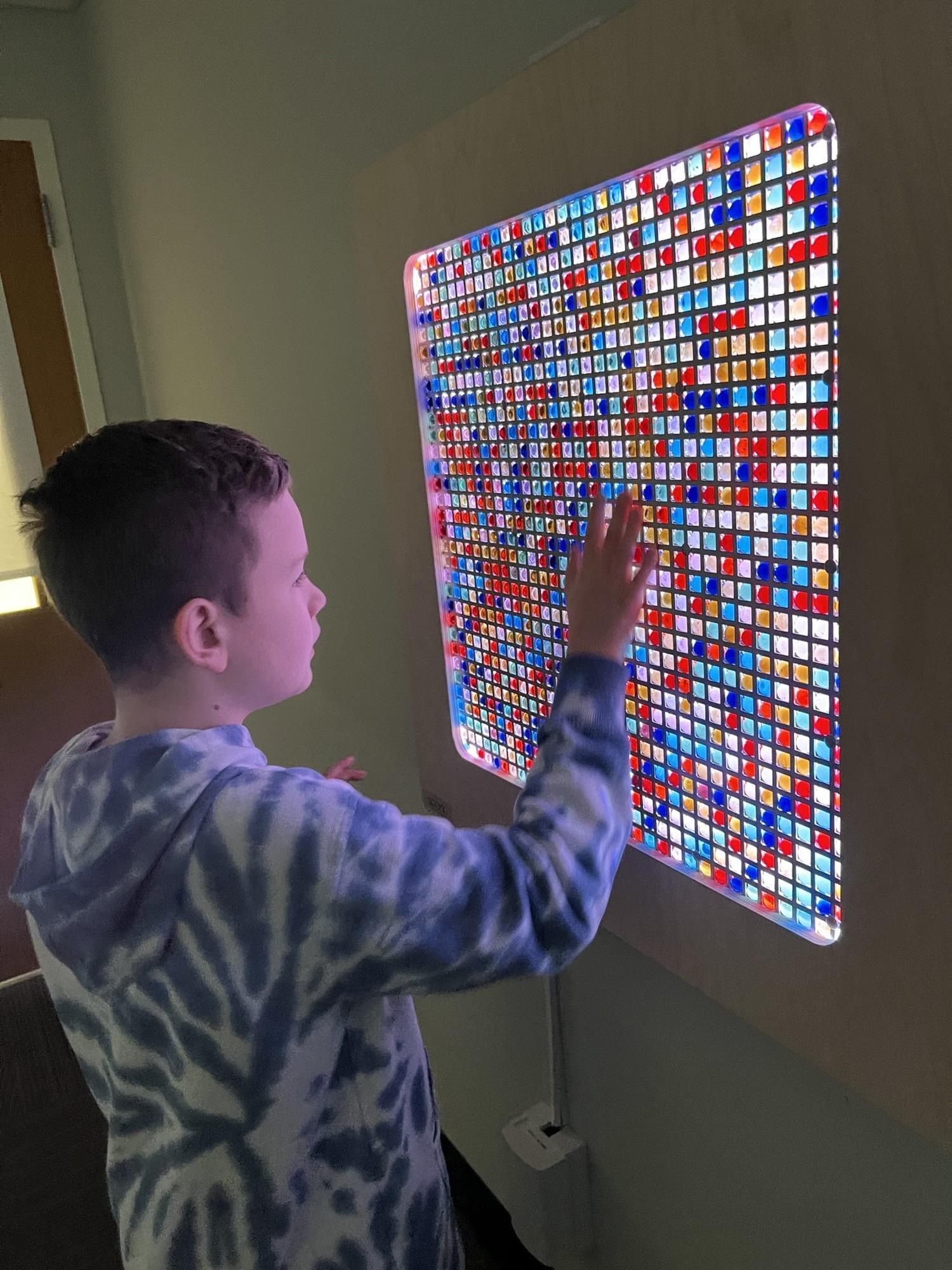 A person touches a square light board filled with small, glowing blue, red, and clear plastic tiles.