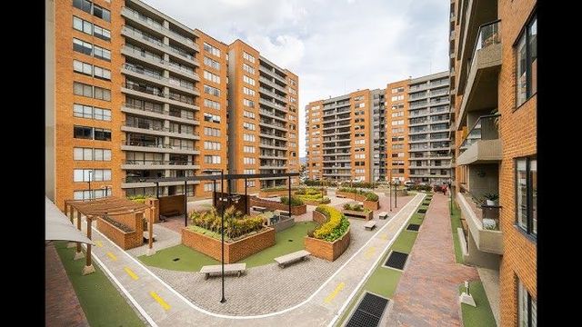 Patio del complejo de apartamentos con zonas verdes, bancos y senderos. Edificios de ladrillo rodean la zona.