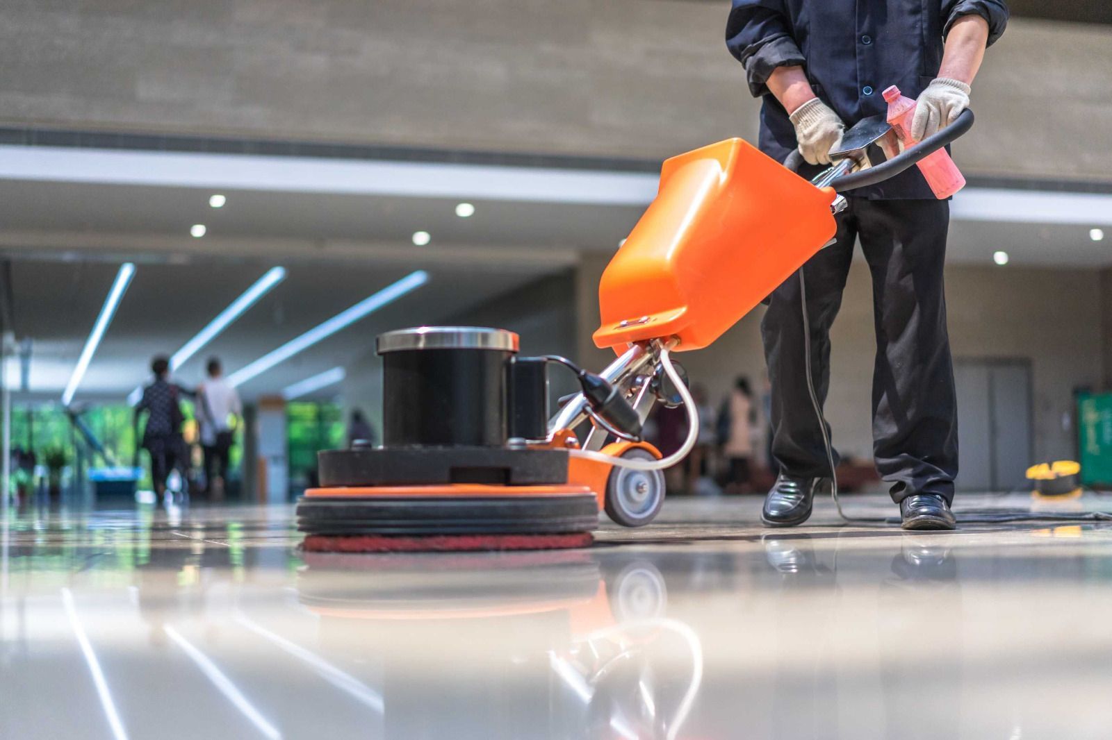 Person operating a floor buffer in a large, shiny hallway.
