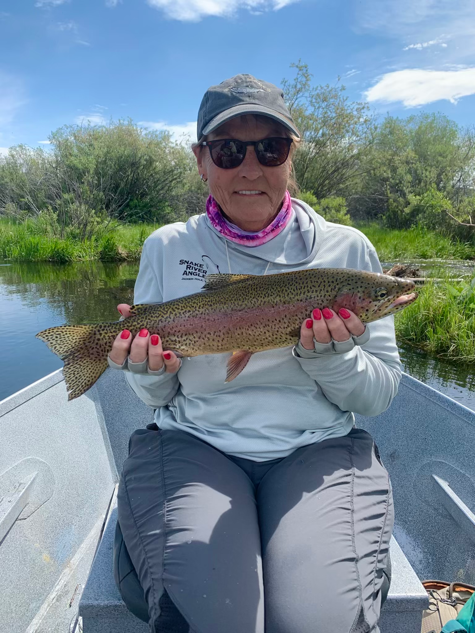 A woman is sitting on a boat holding a rainbow trout.