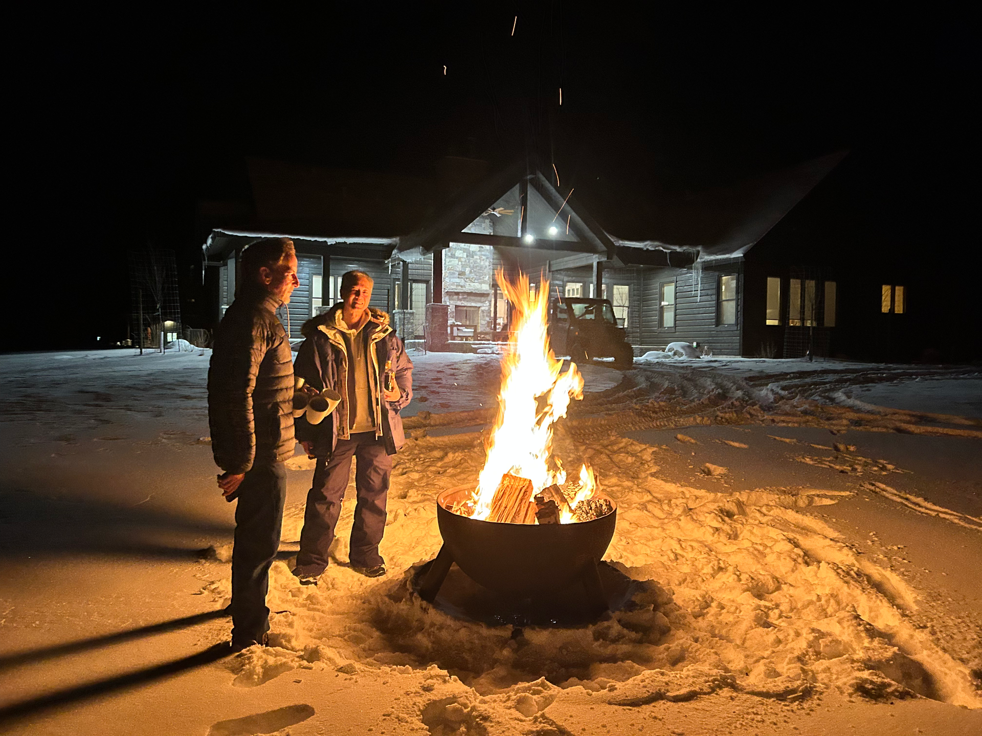 Two people standing next to a fire pit in the snow