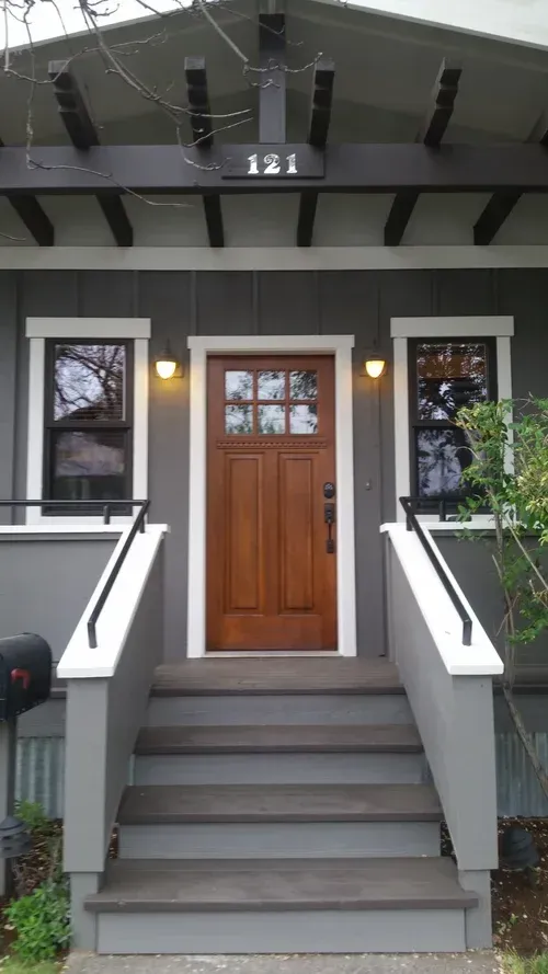 Gray house with wooden door and steps; two windows flank door.