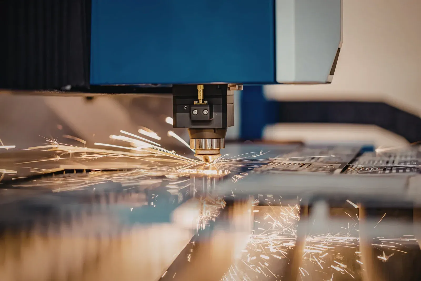 Laser cutter in operation, sparks flying from metal sheet, blue machine.