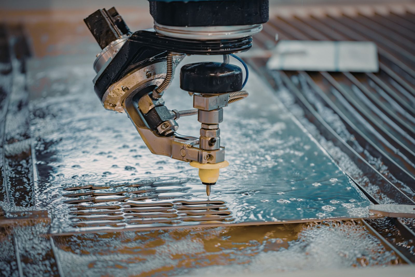 Water jet cutting metal sheet; machine head, silver and black, cuts a pattern.